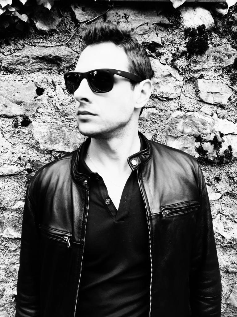 Black-and-white portrait of Jake Marold in sunglasses and a leather jacket against a stone wall
