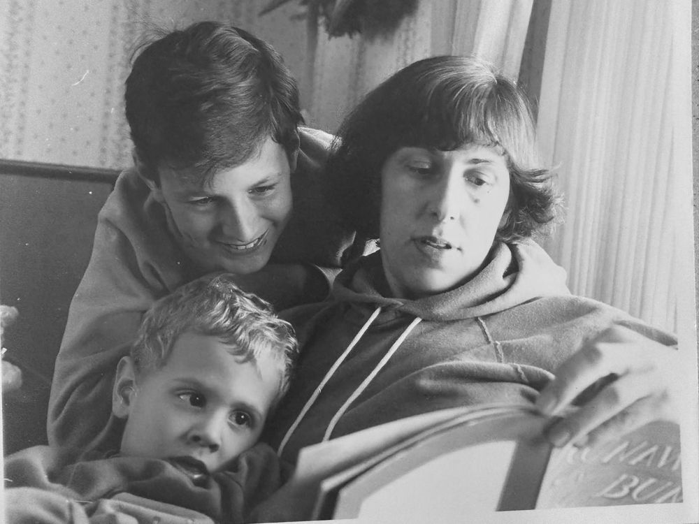 Vintage black-and-white photo of a mother reading a picture book aloud to her two young sons